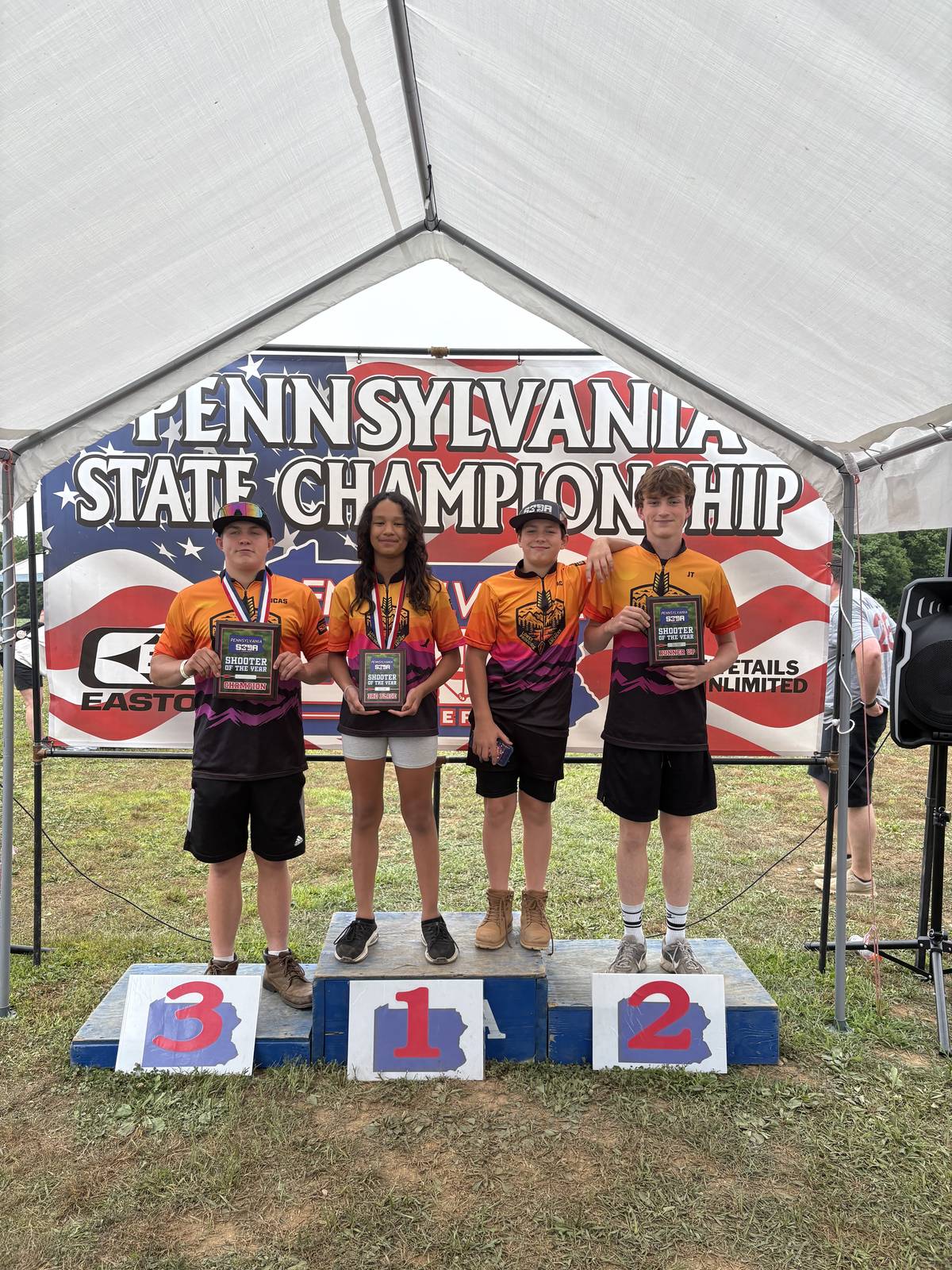 Four LPRGC archers standing on an outdoor podium holding Shooter of the Year plaques under a Pennsylvania State Championship banner.